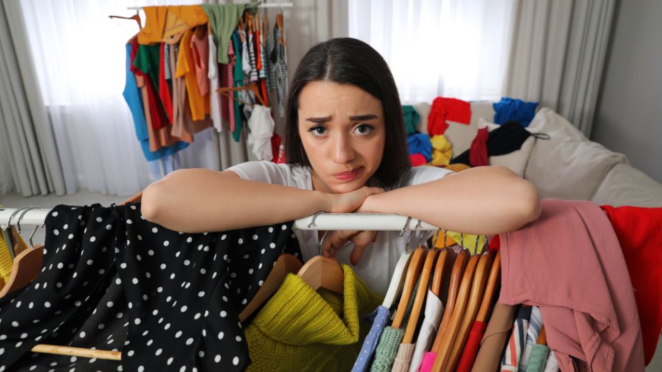 a woman looking overwhelmed by all of the clothes she has in her room