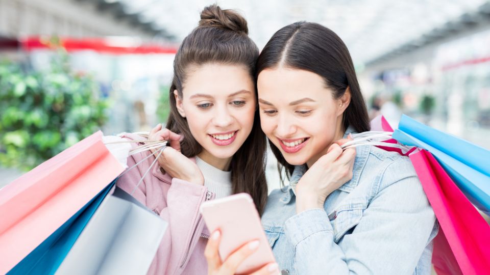 two young women shopping with lots of shopping bags while looking at their phone