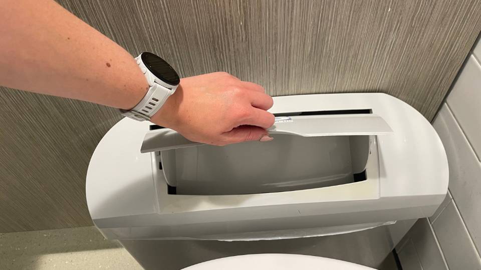 a woman opening a sanitary waste bin in a toilet cubicle