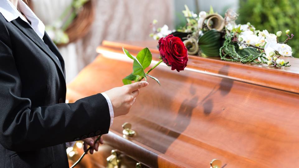 funeral home person holding rose with coffin