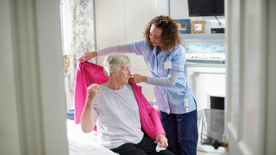 a nurse putting a cardigan on an old lady 