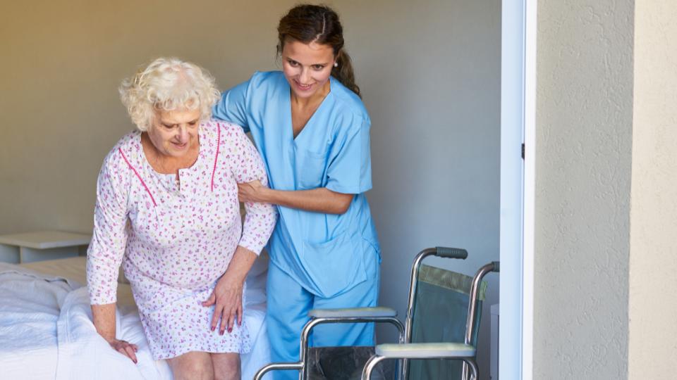 a nurse helping an elderly woman out of her care home bed