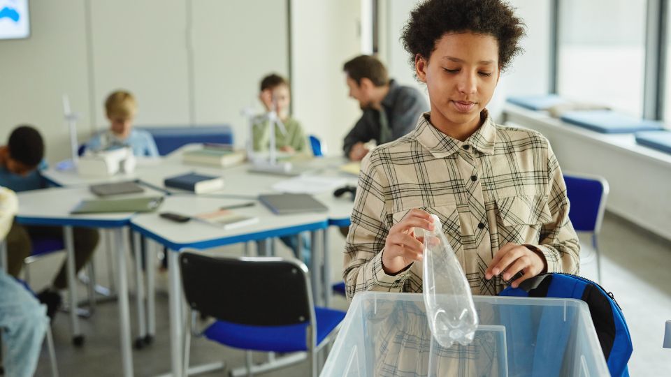 child in UK school putting plastic waste in a dry mixed recycling bin