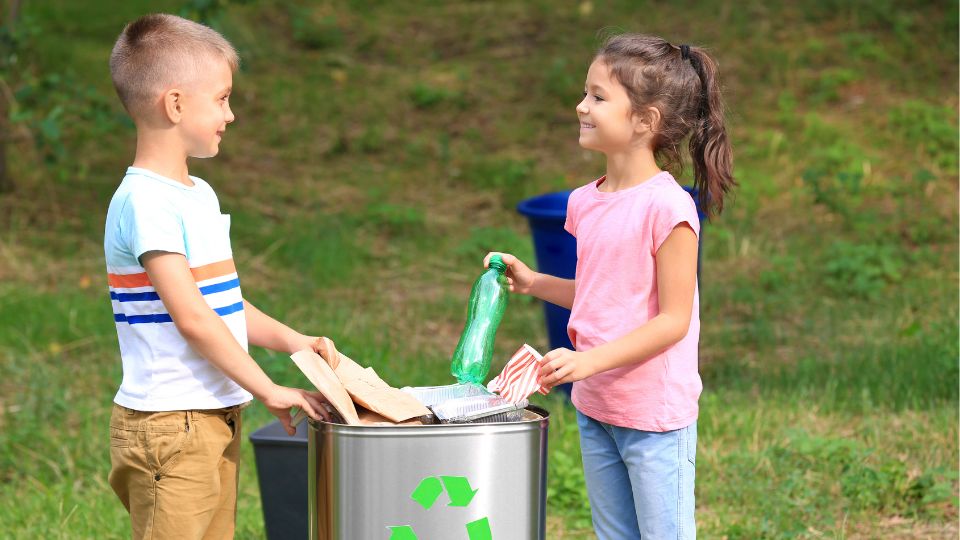 Two children placing plastic and paper into a recycling bin.