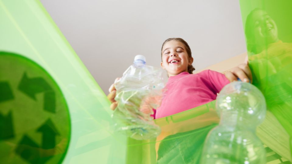 A young girl placing plastic bottles into the recycling bin.