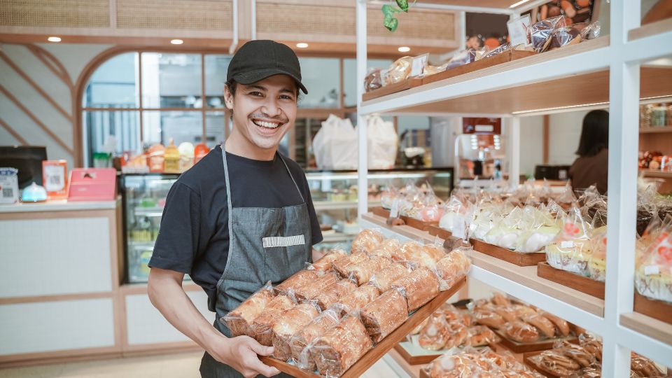 Bakery staff member holding loafs of bread wrapped in plastic