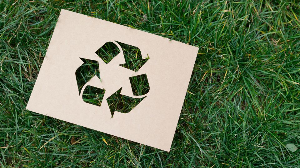A recycling symbol on a piece of paper which is lay out on the grass.