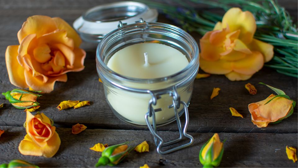 A candle in a small glass jar surrounded by yellow roses.