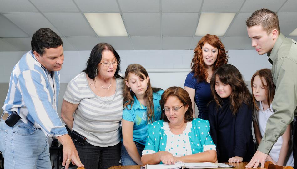 A group of parents and children standing around a teacher who is educating them on something.