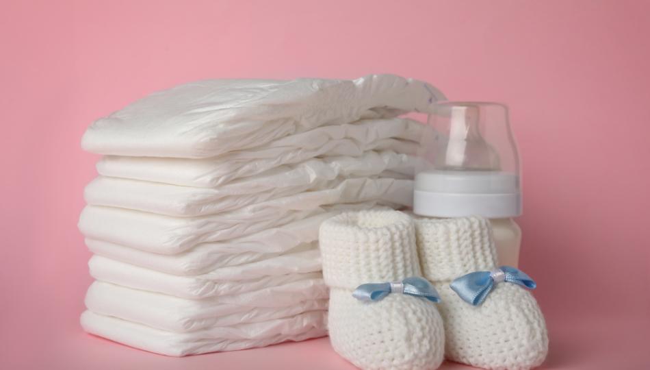 A stack of nappies, a baby bottle and baby shoes, on a pink background