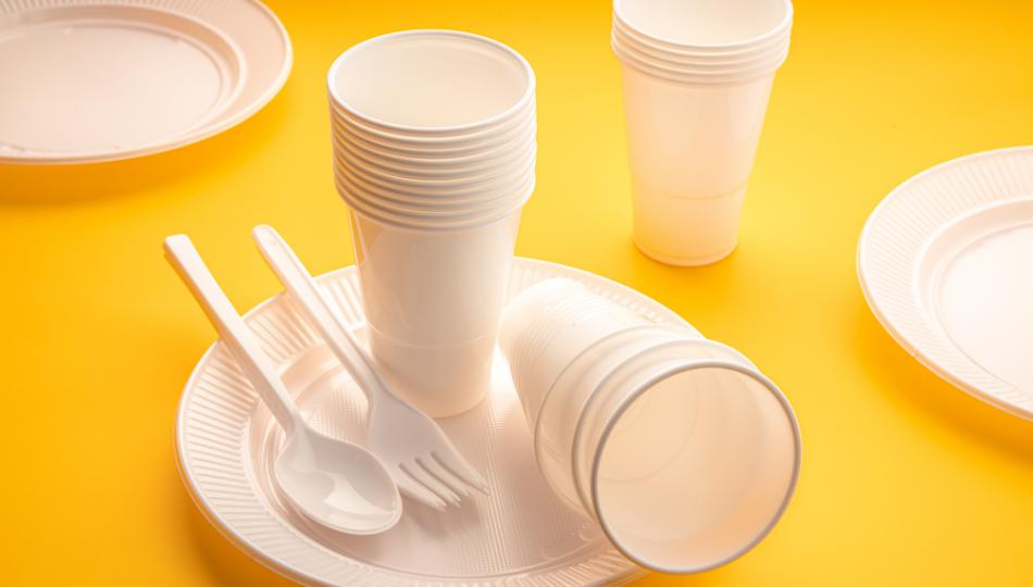 Plastic cutlery including spoons, cups and plates on a yellow background