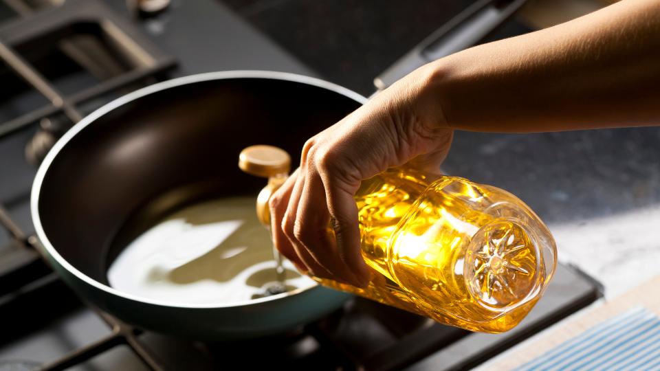 A picture of someone putting cooking oil into a pan