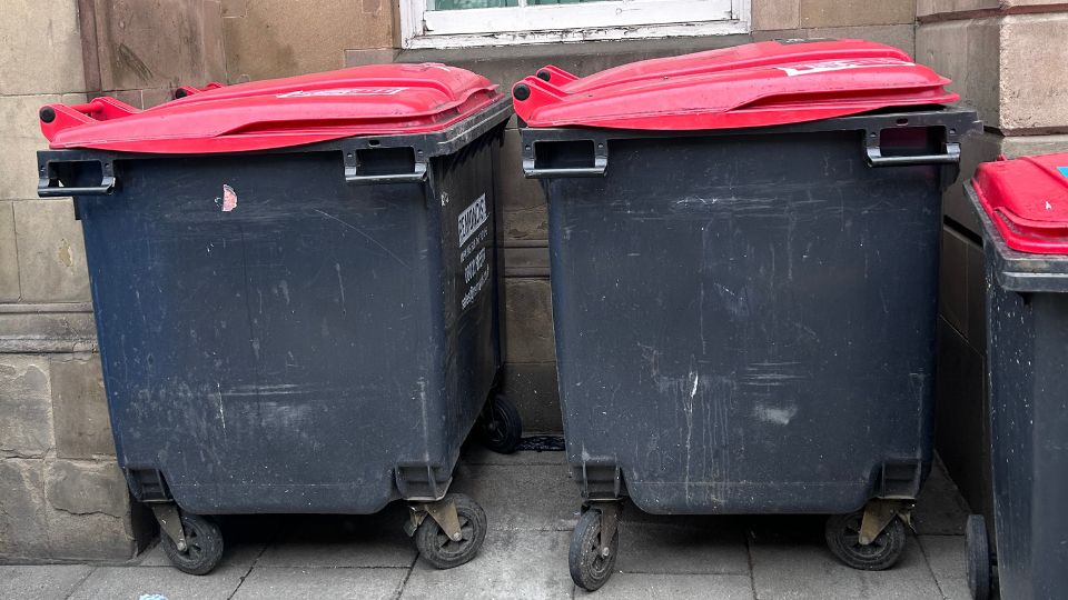 Two 1100L black wheelie bins with red lids